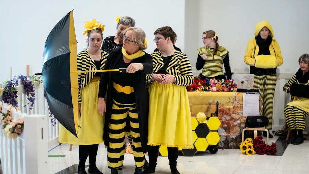 A group of dancers dressed in yellow and black reminiscent of bees perform with umbrella