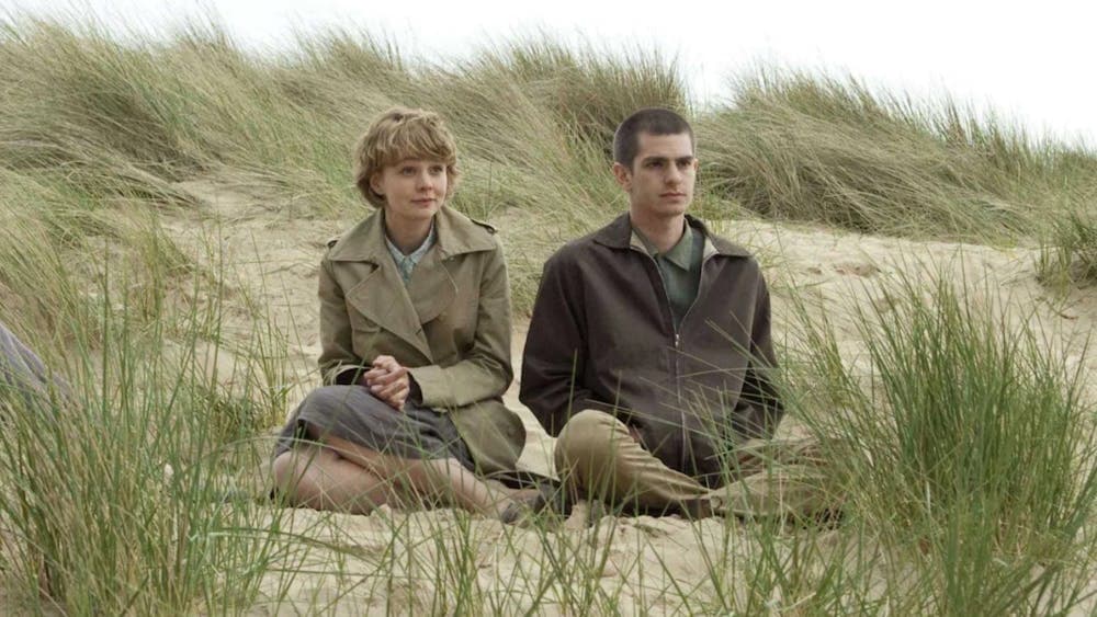 One woman and one man sitting rugged up in coats on a beach
