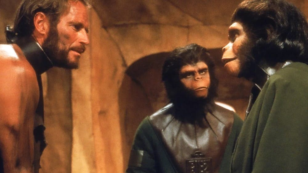 Two ape looking figures facing a man wearing a metal collar