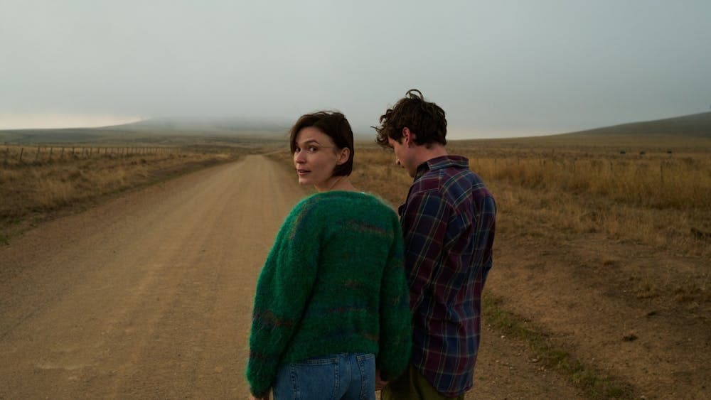 Young woman and man pictured in a flat field, woman looks back at camera