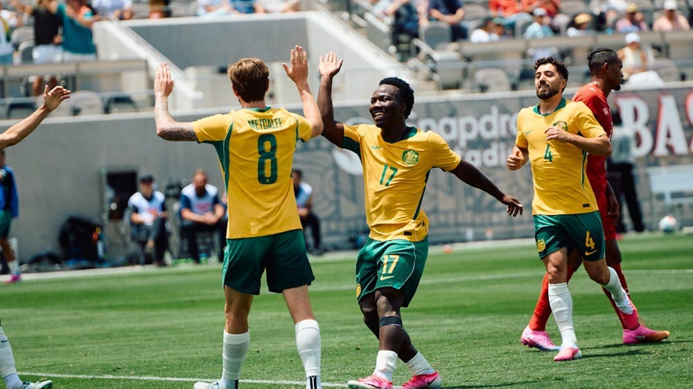 Soccer players in yellow kits celebrate a goal on a stadium pitch as teammates run in behind