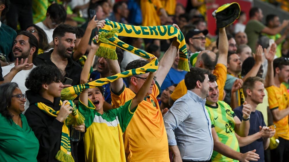 Soccer players in yellow kits celebrate a goal on a stadium pitch as teammates run in behind