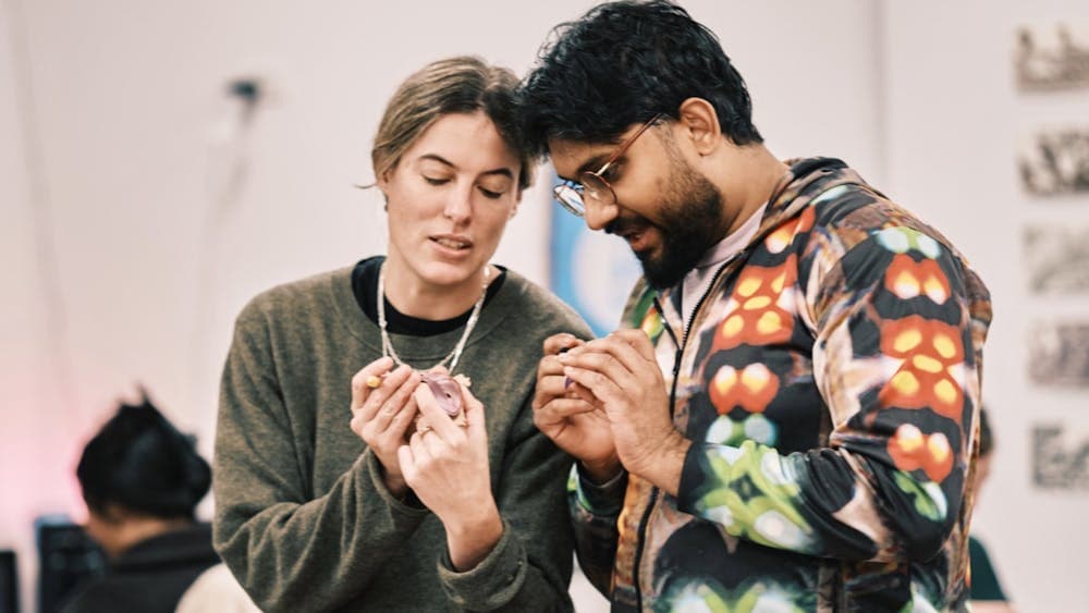 Two people examining handmade artwork pendants closely at a craft event.